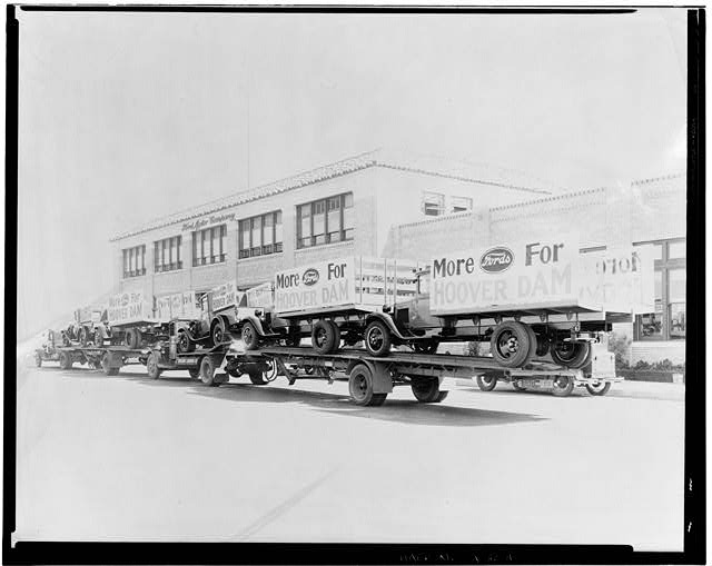 Ford Long Beach Assembly Plant Sep 24, 1931, EXTERIOR-OFFICE BUILDING AND ASSEMBLY BUILDING, WEST SIDE, SHOWING TRUCKS AND TRAILORS LOADED WITH NEW TRUCKS DISPLAYING SIGNS MORE FORDS FOR HOOVER DAM