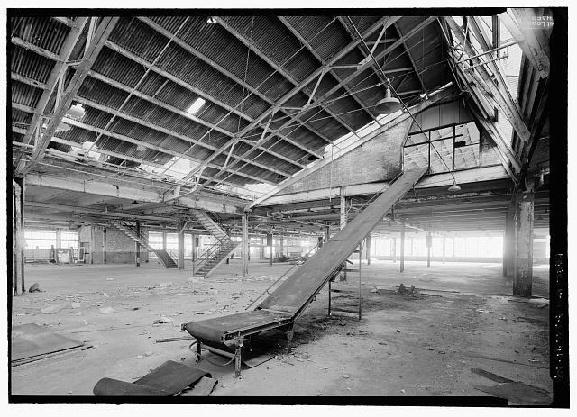 Ford Richmond Assembly Plant VIEW TO SOUTHWEST OF FIRST FLOOR SHOWING CONVEYOR FOR MOVING MATERIAL TO SECOND FLOOR. (NOTE: THIS IS NOT AN ORIGINAL CONVEYOR FOR MOVING BODY PARTS) STAIRS IN BACKGROUND LEAD TO SECOND FLOOR VIA TOILET ROOM NO. 4 AND COAT ROOM AT MEZZANINES LEVEL SITUATED BETWEEN THE TWO SETS OF STAIRS. THERE ARE THREE OTHER TOILET/COAT ROOM MEZZANINES TO THE NORTH LOCATED ALONG THE WALL BETWEEN THE FIRST AND SECOND FLOORS, BEHIND AND TO THE LEFT OF THE STAIRS IS A FREIGHT ELEVATOR SHAFT.